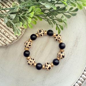 May include: A black and gold beaded bracelet with a leopard print design.