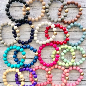 May include: A collection of 10 colorful wooden bead bracelets with gold accents. Each bracelet features a different color, including turquoise, pink, red, white, and blue.