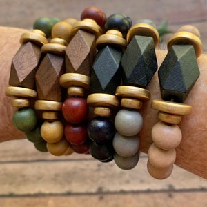 May include: A set of six bracelets featuring wooden beads in various colors, including brown, black, green, and gold. The beads are arranged in a repeating pattern, creating a visually appealing and stylish design.