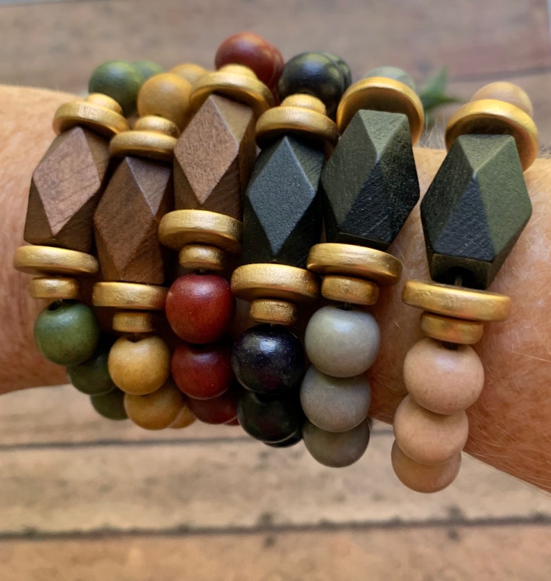 May include: A set of six bracelets featuring wooden beads in various colors, including brown, black, green, and gold. The beads are arranged in a repeating pattern, creating a visually appealing and stylish design.