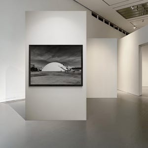 Puede incluir: Fotograf&iacute;a en blanco y negro de un edificio con un gran techo blanco en forma de c&uacute;pula, enmarcada en un marco negro, colgada en una pared blanca de una galer&iacute;a. La galer&iacute;a tiene paredes blancas y suelo gris.