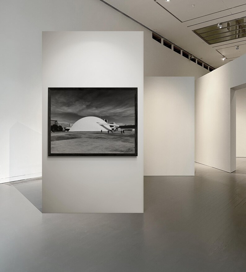Puede incluir: Fotograf&iacute;a en blanco y negro de un edificio con un gran techo blanco en forma de c&uacute;pula, enmarcada en un marco negro, colgada en una pared blanca de una galer&iacute;a. La galer&iacute;a tiene paredes blancas y suelo gris.