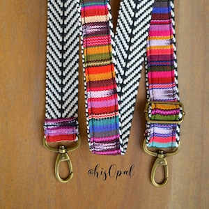 May include: A black and white chevron patterned strap with a colourful woven stripe down the centre. The strap has two brass clasps.