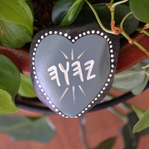 May include: A grey heart-shaped rock with white polka dots and the word "Zefz" written in white paint.
