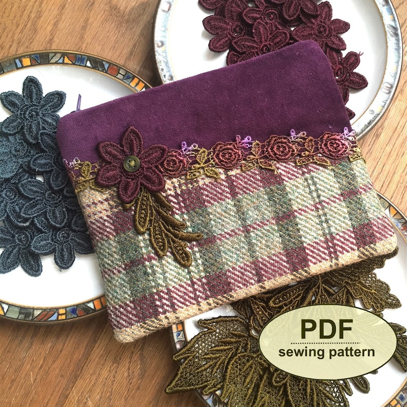 K&ouml;nnte beinhalten: Eine Stofftasche mit einem dunkelvioletten Wildleder-Oberteil und einem Karomuster, verziert mit floraler Spitze und einem Knopf. Spitzenblumen in Gr&uuml;n, Burgunderrot und Teal liegen auf Tellern. Thema: N&auml;hvorlage.