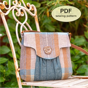 Peut inclure: Un patron de couture PDF pour un sac bandoulière en tissu à carreaux avec une bandoulière en cuir marron et un bouton en forme de rose. Le sac est posé sur une chaise en métal blanc.