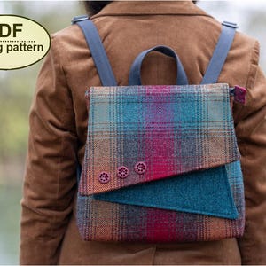 Könnte beinhalten: Ein karierter Rucksack in Blau-, Türkis-, Rosa- und Brauntönen. Der Überschlag hat drei dekorative Knöpfe. Der Text "PDF sewing pattern" befindet sich in einem gelben Oval. Der Rucksack hat blaue Träger.