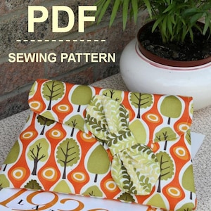 May include: A PDF sewing pattern for a clutch purse with a bow. The clutch is made of fabric with a green, orange, and white pattern of trees. The pattern is available as a digital download.