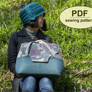 May include: A teal blue felt bag with a floral patterned flap and a teal blue felt hat with a button detail. The bag and hat are sitting on a bed of green grass and purple flowers. The text "PDF sewing pattern" is written in a brown oval on the image.