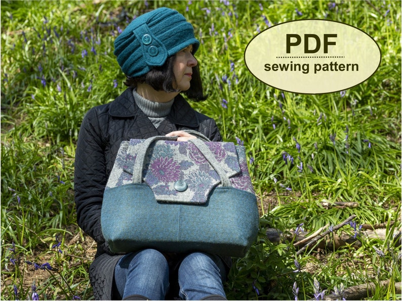 May include: A teal blue felt bag with a floral patterned flap and a teal blue felt hat with a button detail. The bag and hat are sitting on a bed of green grass and purple flowers. The text "PDF sewing pattern" is written in a brown oval on the image.