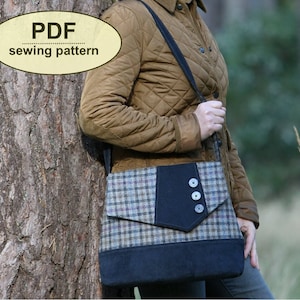 May include: A PDF sewing pattern for a shoulder bag featuring a plaid fabric body with a dark blue flap and base. The flap is accented with a dark blue vertical panel and three round buttons. The bag has a long shoulder strap and a rectangular shape.