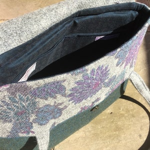 May include: A gray and green tweed tote bag with a floral pattern and a dark blue lining. The bag has a single strap and a button closure.