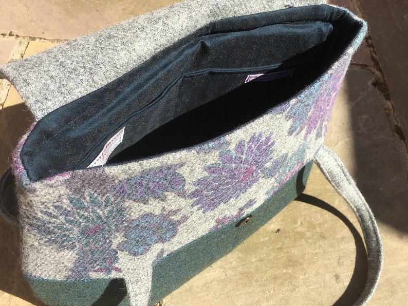 May include: A gray and green tweed tote bag with a floral pattern and a dark blue lining. The bag has a single strap and a button closure.