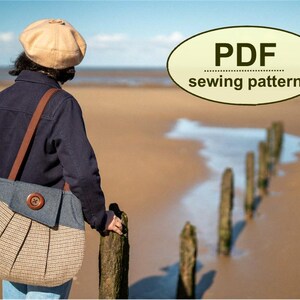 K&ouml;nnte beinhalten: Eine Person am Strand mit einer marineblauen Jacke und einer beigefarbenen und Jeans-Umh&auml;ngetasche mit einem Holzknopf. Die Tasche hat ein plissiertes Design. Das Bild enth&auml;lt eine Text&uuml;berlagerung mit der Aufschrift "PDF sewing pattern".