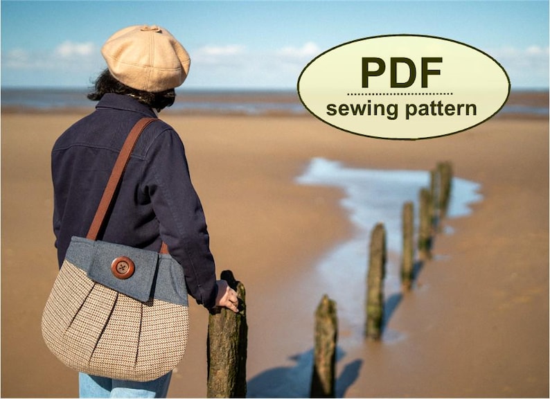K&ouml;nnte beinhalten: Eine Person am Strand mit einer marineblauen Jacke und einer beigefarbenen und Jeans-Umh&auml;ngetasche mit einem Holzknopf. Die Tasche hat ein plissiertes Design. Das Bild enth&auml;lt eine Text&uuml;berlagerung mit der Aufschrift "PDF sewing pattern".