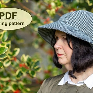 May include: A woman wearing a black and white checked hat with a wide brim. The hat is a sewing pattern available as a PDF download. The woman is standing in front of a bush with green and yellow leaves and red berries.