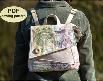 May include: A beige and multi-colored backpack with a flap closure, featuring a vintage-style print with butterflies and text. The backpack has adjustable straps and a top handle. The text "SUCHARD" is visible on the front. A button closure secures the flap.