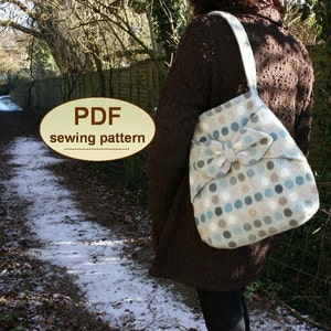 Può includere: Un cartamodello PDF per una grande borsa a tracolla con un dettaglio a fiocco. La borsa è realizzata in tessuto blu chiaro con un motivo a pois bianchi e marroni. La borsa viene indossata da una persona con un maglione marrone.