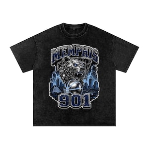 May include: Black t-shirt with a distressed wash featuring a graphic of a bear with a basketball, the word "MEMPHIS" above, and "901" below. The design includes a cityscape and lightning bolts in blue and white.