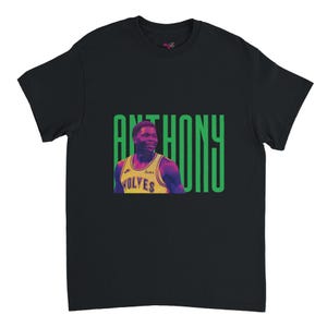 Pode incluir: Camiseta preta com um gráfico de um jogador de basquete em uma camisa amarela. A palavra "ANTHONY" está em letras verdes. A camisa tem a palavra "WOLVES".