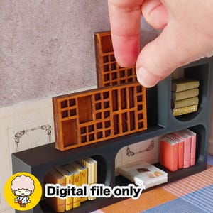May include: Miniature wooden bookshelf with a dark blue frame and various tiny books in yellow, pink, and white. The bookshelf has a decorative wooden insert being placed. The text "Digital file only" is visible.