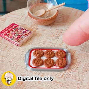Pode incluir: Cena em miniatura com uma bandeja de seis biscoitos castanhos, um livro de receitas, uma tigela de madeira e uma colher. O livro de receitas é intitulado "Candy Cookbooks COOKIE BOOK". O texto "Digital file only" também é visível.