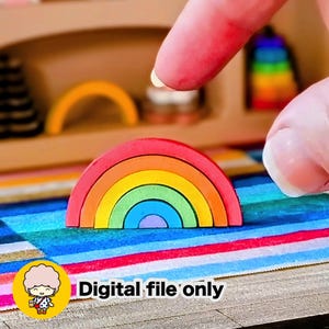 Puede incluir: Un juguete de arcoíris de madera con arcos rojos, naranjas, amarillos, verdes y azules. El juguete está sobre una superficie a rayas. El texto "Digital file only" es visible en la imagen.
