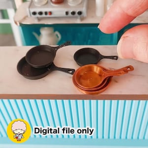 Może przedstawiać: Kolekcja miniaturowych naczyń kuchennych do domku dla lalek, w tym dwie czarne patelnie i dwie patelnie w kolorze miedzi ułożone na białej powierzchni. Obraz zawiera żółtą ikonę z postacią z kreskówki oraz tekst Digital file only.