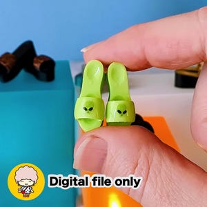 May include: A pair of miniature lime green sandals with alien face graphics. The sandals are held up by a hand. The text "Digital file only" is in the lower right corner.