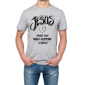 Puede incluir: Camiseta gris claro con la palabra "JESUS" en negro, escrita a mano. Debajo, un coraz&oacute;n con una cruz y el texto "PROOF THAT TABLE-FLIPPING is biblical".