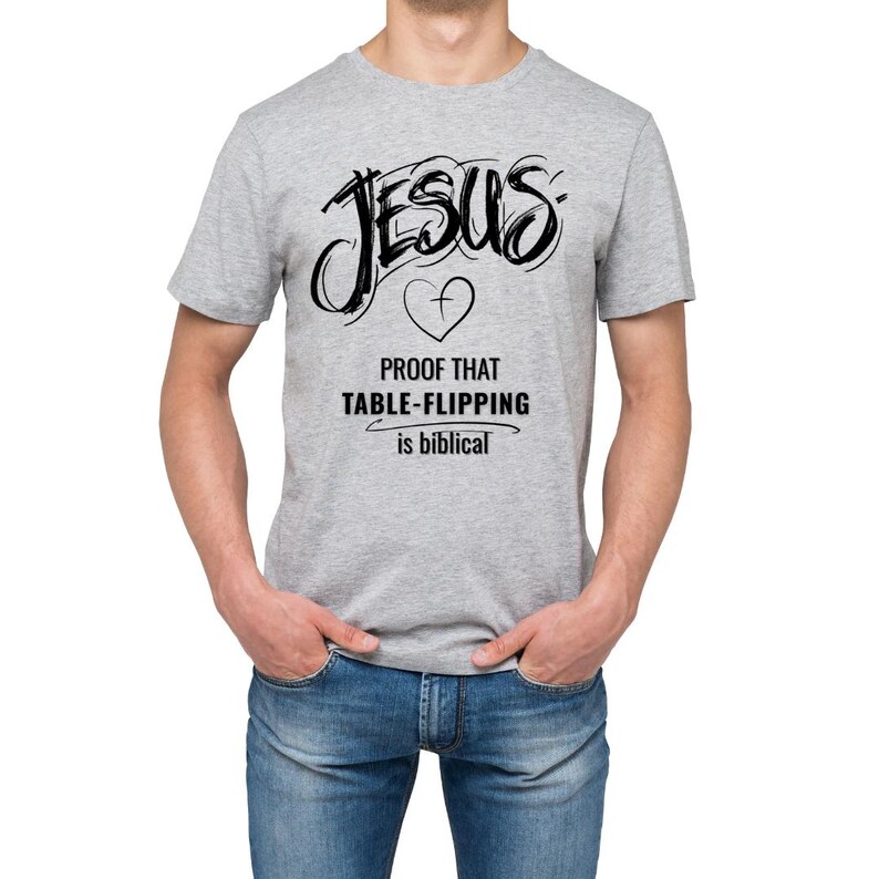 Puede incluir: Camiseta gris claro con la palabra "JESUS" en negro, escrita a mano. Debajo, un coraz&oacute;n con una cruz y el texto "PROOF THAT TABLE-FLIPPING is biblical".