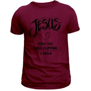 Puede incluir: Camiseta burdeos con la palabra "Jes&uacute;s" en escritura negra, un s&iacute;mbolo de coraz&oacute;n y el texto "PROOF THAT TABLE-FLIPPING is biblical". La camiseta tiene cuello redondo y mangas cortas.