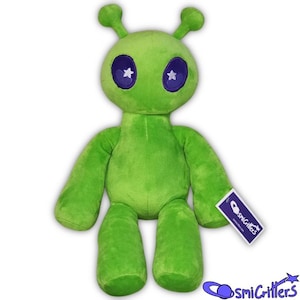 Puede incluir: Un peluche verde con forma de alienígena con grandes ojos morados y pupilas en forma de estrella. El alienígena tiene pequeñas antenas y una etiqueta que dice "CosmiCritters". El peluche es suave y adecuado para niños o coleccionistas.