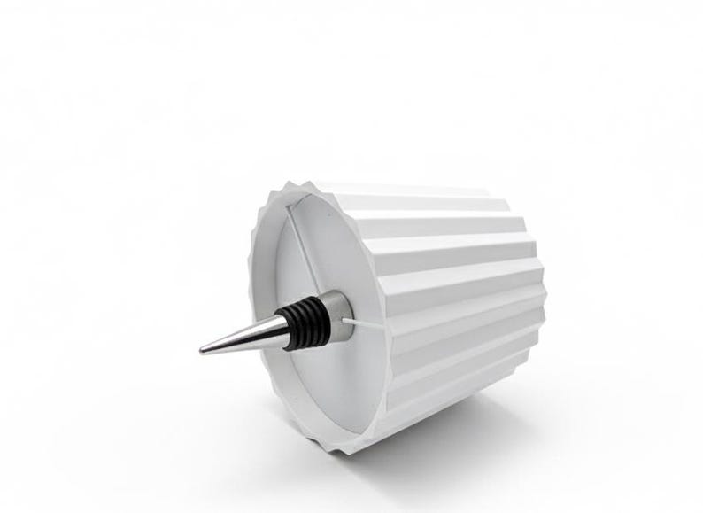 May include: A white wine bottle stopper with a geometric design. The stopper has a silver-coloured, conical tip and a black rubber seal. The white container has a ridged, cylindrical shape.