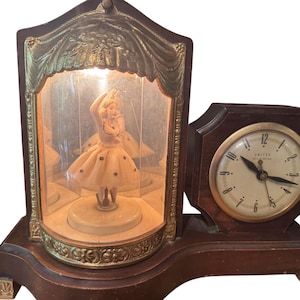 May include: An antique wooden clock with a built-in ballerina figurine display. The clock features a round face with the word "Salter" and a decorative gold-toned frame. The ballerina is in a glass enclosure.