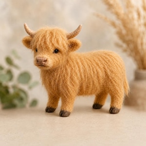 Peut inclure: Figurine miniature faite &agrave; la main repr&eacute;sentant une vache des Highlands. Le jouet en peluche est de couleur brun dor&eacute; chaud, avec de petites cornes incurv&eacute;es et des sabots fonc&eacute;s. La vache est sur une surface neutre.