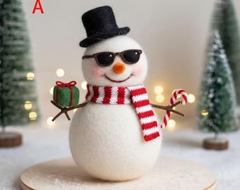 May include: A white felt snowman figurine wearing a black top hat and dark sunglasses. The snowman has a small orange nose, a red and white striped scarf, and holds a green gift box in one hand and a red and white candy cane in the other.