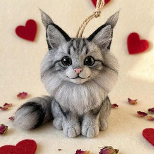 May include: A handcrafted gray and white cat figurine with large, dark eyes and a pink nose. The cat has a fluffy mane and tail, and is adorned with a jute string for hanging. Red felt hearts and rose petals are scattered around the cat.