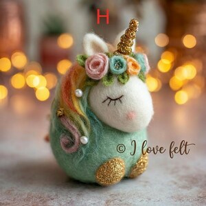 Op de afbeelding: Een vilten eenhoornfiguur met een wit gezicht, gesloten ogen en een roze neus. Het heeft een gouden hoorn, een bloemenkrans en een regenboogmanen. De body is groen met gouden glitteraccenten. De tekst "&copy; I love felt" is zichtbaar.
