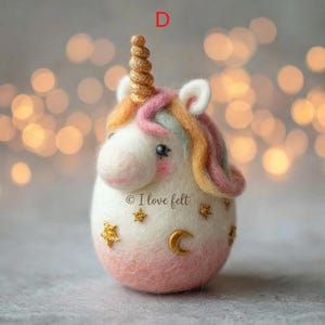 Op de afbeelding: Een handgemaakt vilten eenhoornbeeldje met een gouden hoorn, veelkleurige manen en roze wangen. Het witte lichaam gaat over in zachtroze aan de basis, versierd met gouden sterren en een maan. De tekst "I love felt" is zichtbaar.
