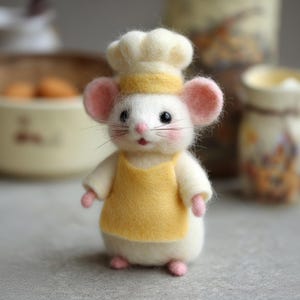 Pu&ograve; includere: Figurina di topo in feltro fatta a mano vestita da chef. Il topo indossa un cappello da chef bianco con una fascia gialla, un grembiule giallo e un'uniforme bianca. Ha orecchie, naso e piedi rosa, con occhi neri e baffi. La figurina &egrave; in piedi.