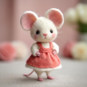 Pu&ograve; includere: Una figura di topo in feltro fatta a mano con corpo bianco, grandi orecchie foderate di rosa e naso rosa. Indossa un vestito color corallo con scarpe abbinate. Il topo ha delicati baffi e guance rosee.