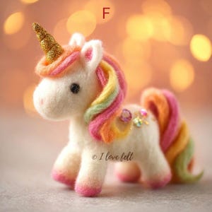 Op de afbeelding: Handgemaakte eenhoornfiguur van vilt met een gouden hoorn, regenboogmanen en -staart. De eenhoorn heeft roze hoeven en is versierd met glinsterende edelstenen. De tekst "I love felt" is zichtbaar.