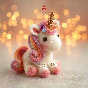Op de afbeelding: Een handgemaakte vilten eenhoorn met een gouden glitterhoorn, regenboogmanen en -staart en roze hoeven. De eenhoorn heeft een wit lichaam, kleine bruine ogen en is versierd met kleine bloemen en edelsteenaccenten. De tekst "I love felt" is zichtbaar.