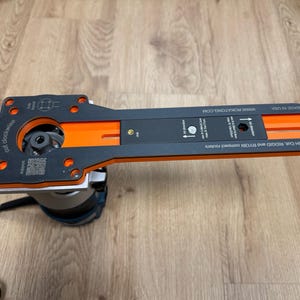 Puede incluir: Una plantilla de enrutador negra y naranja con el texto "cut clockwise" y "www.ROKATONG.COM". La plantilla est&aacute; unida a una base de enrutador. Tambi&eacute;n es visible el texto "For BOSH COIL, RIDGID and RYOBI compact routers".