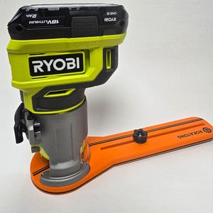 May include: A cordless power router with a bright green and black body, featuring the brand name "RYOBI". It is attached to an orange base with the text "ROKATONG". The router is designed for woodworking and DIY projects.
