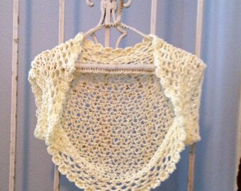 May include: A crocheted cream-colored shrug with a scalloped edge. The shrug is hanging on a white metal hanger.