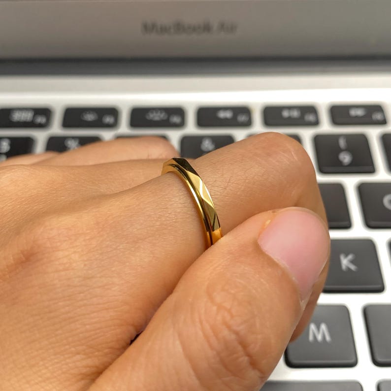 May include: A gold-colored ring with a geometric design. The ring is worn on a finger, showcasing its polished surface and angular facets. The ring's design reflects light, creating a bright and eye-catching appearance. Jewelry.