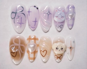 May include: A set of ten artificial nails with various designs. The nails feature a mix of pastel colors, including lavender and brown, with decorative elements such as bows, hearts, and a cartoon cat and dog. Some nails have glitter accents.
