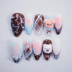 May include: A set of ten almond-shaped artificial nails with various designs. The designs include stars, bows, plaid patterns, a puppy, a cat, and musical notes. Colors include brown, white, pink, and blue, with pearl accents.